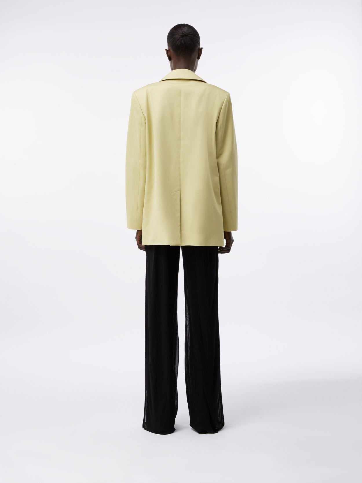 model wearing a pale olive square blazer and draped trousers with twist detail