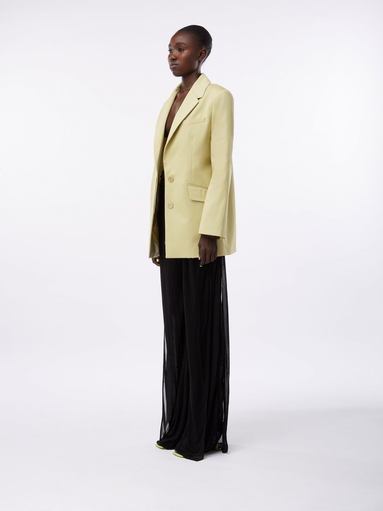 model wearing a pale olive square blazer and draped trousers with twist detail